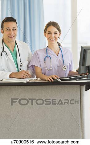 Stock Photograph - Portrait of male and female nurses at nurse's station in hospital. Fotosearch
