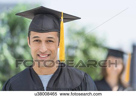 Stock Photography - Portrait of male student on graduation ceremony with female student in background. Fotosearch