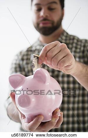 Portrait of man holding piggy ban and putting money inside View Large Photo Image Picture - Portrait of man holding piggy ban and putting money inside. Fotosearch