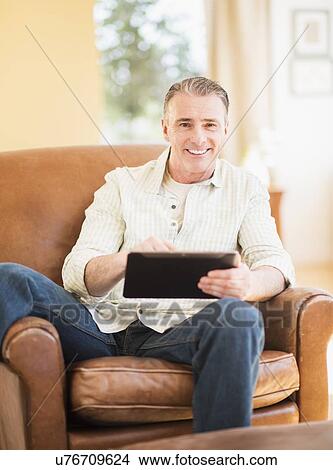 Picture - Portrait of man in armchair using digital tablet. Fotosearch