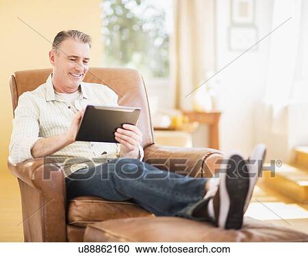 Portrait of man in armchair using digital tablet View Large Photo Image Stock Image - Portrait of man in armchair using digital tablet. Fotosearch
