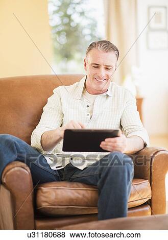 Stock Photo - Portrait of man in armchair using digital tablet. Fotosearch