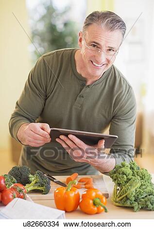 Picture - Portrait of man in kitchen, holding digital tablet. Fotosearch
