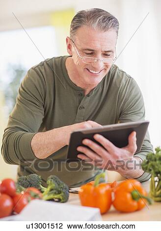 Portrait of man in kitchen, holding digital tablet View Large Photo Image Stock Image - Portrait of man in kitchen, holding digital tablet. Fotosearch