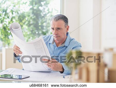 Stock Image - Portrait of man looking at blueprints in office. Fotosearch