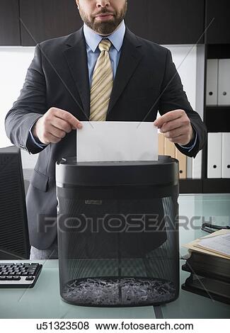 Stock Photo - Portrait of man putting paper into paper shredder. Fotosearch