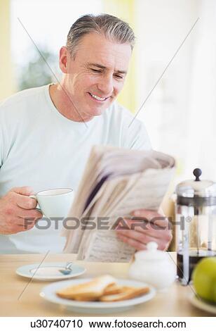 Stock Image - Portrait of man reading newspaper and having breakfast. Fotosearch