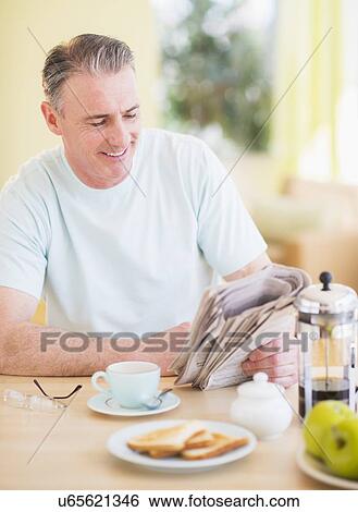 Stock Photograph - Portrait of man reading newspaper and having breakfast. Fotosearch