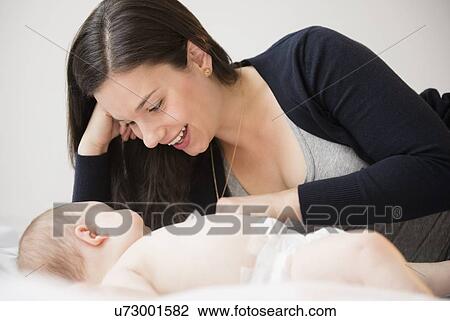 Stock Image - Portrait of mother and baby daughter (6-11 months) lying in bed. Fotosearch