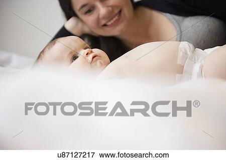 Stock Photo - Portrait of mother and baby daughter (6-11 months) lying in bed. Fotosearch