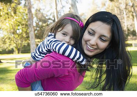 Stock Image - Portrait of mother giving her daughter (4-5) piggy back ride in park. Fotosearch