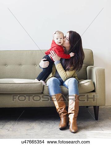 Portrait of mother sitting on sofa and kissing her daughter (12-17 months) View Large Photo Image Picture - Portrait of mother sitting on sofa and kissing her daughter (12-17 months). Fotosearch