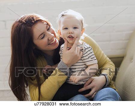 Portrait of mother sitting on sofa and touching face of her daughter's (12-17 months) View Large Photo Image Stock Image - Portrait of mother sitting on sofa and touching face of her daughter's (12-17 months). Fotosearch