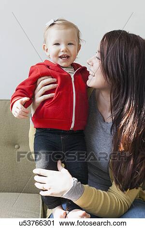 Stock Image - Portrait of mother sitting on sofa with her daughter (12-17 months). Fotosearch