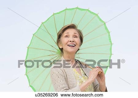 Stock Photograph - Portrait of senior woman holding green parasol. Fotosearch