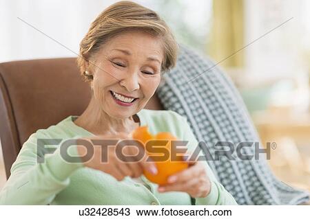 Stock Image - Portrait of senior woman peeling orange. Fotosearch
