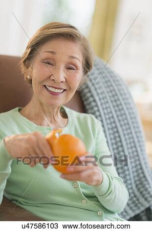 Stock Image - Portrait of senior woman peeling orange. Fotosearch