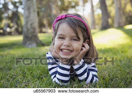 Stock Image - Portrait of smiling girl (4-5 years) lying on grass in park. Fotosearch