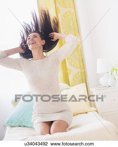 Stock Image - Portrait of woman kneeling on bed with hair tousled. Fotosearch
