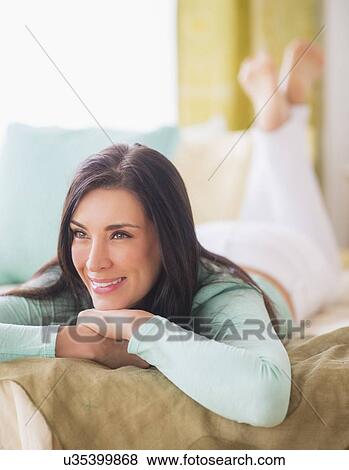 Stock Photo - Portrait of woman lying down on bed with hand on chin, Looking away, Close-up. Fotosearch