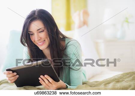 Portrait of woman lying down on bed using tablet pc View Large Photo Image Stock Photo - Portrait of woman lying down on bed using tablet pc. Fotosearch