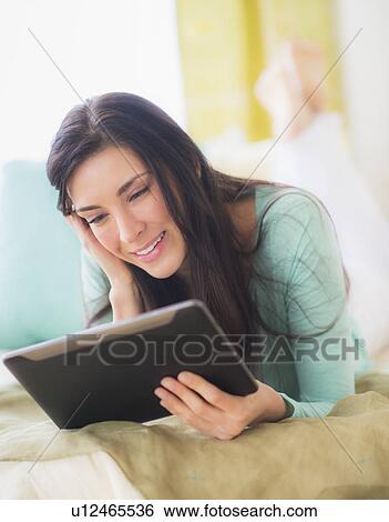 Stock Photograph - Portrait of woman lying down on bed using tablet pc, Close-up. Fotosearch