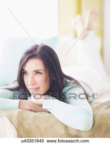Stock Photography - Portrait of woman lying down on bed with hand on chin, Looking away, Close-up. Fotosearch