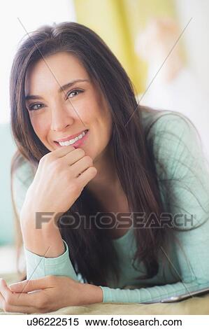 Stock Photography - Portrait of woman lying down on bed with hand on chin, Close-up. Fotosearch