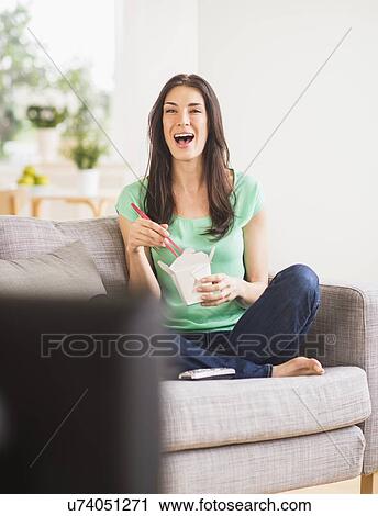 Stock Image - Portrait of woman watching tv and eating take out food. Fotosearch