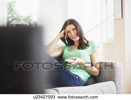 Stock Image - Portrait of woman watching TV on sofa. Fotosearch