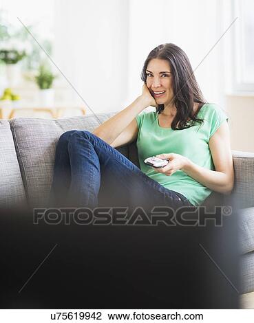 Stock Image - Portrait of woman watching TV on sofa. Fotosearch