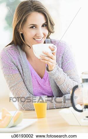 Stock Image - Portrait of young woman drinking tea at table. Fotosearch