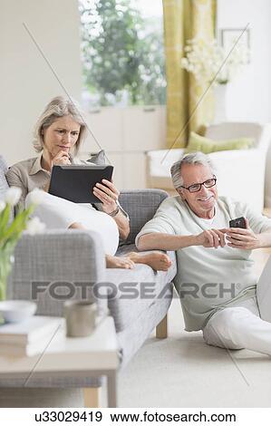 Stock Photo - Senior couple using digital tablet and cell phone at home. Fotosearch