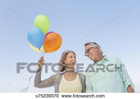 Senior couple with bunch of balloons against clear sky View Large Photo Image Stock Image - Senior couple with bunch of balloons against clear sky. Fotosearch