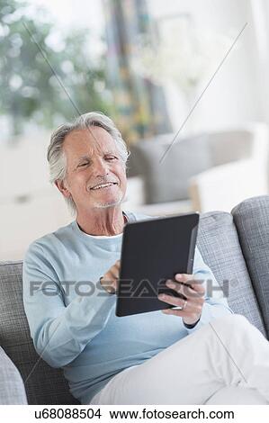 Picture - Senior man sitting on sofa with digital tablet. Fotosearch