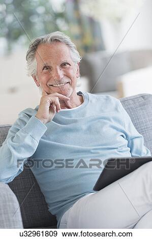 Senior man sitting on sofa with digital tablet View Large Photo Image Stock Photo - Senior man sitting on sofa with digital tablet. Fotosearch