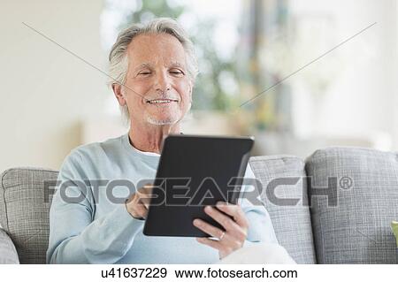 Senior man sitting on sofa with digital tablet View Large Photo Image Stock Photo - Senior man sitting on sofa with digital tablet. Fotosearch