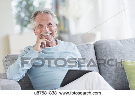 Stock Photo - Senior man sitting on sofa with digital tablet. Fotosearch