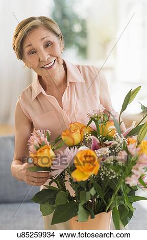 Picture - Senior woman arranging flowers in living room. Fotosearch