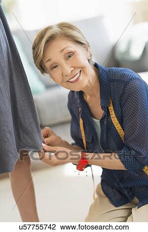 Stock Image - Senior woman attaching sewing pins to girl's (8-9) dress. Fotosearch
