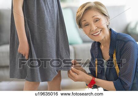 Stock Photograph - Senior woman attaching sewing pins to girl's (8-9) dress. Fotosearch