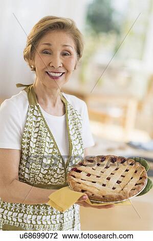 Stock Image - Senior woman holding freshly baked cake. Fotosearch