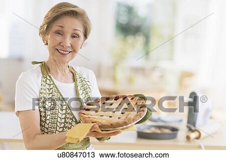Stock Image - Senior woman holding freshly baked cake. Fotosearch