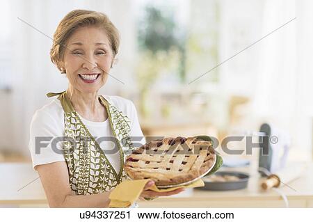 Stock Image - Senior woman holding freshly baked cake. Fotosearch