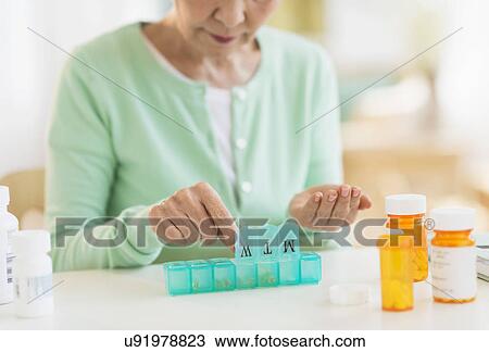 Stock Image - Senior woman organizing medicine in box. Fotosearch