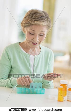 Stock Photo - Senior woman organizing medicine in box. Fotosearch