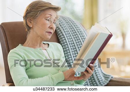 Stock Image - Senior woman reading book at home. Fotosearch