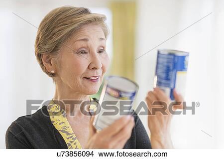 Picture - Senior woman reading labels on canned food. Fotosearch