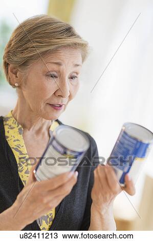 Stock Image - Senior woman reading labels on canned food. Fotosearch