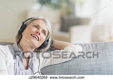 Senior woman sitting on sofa and listening to music View Large Photo Image Stock Photo - Senior woman sitting on sofa and listening to music. Fotosearch